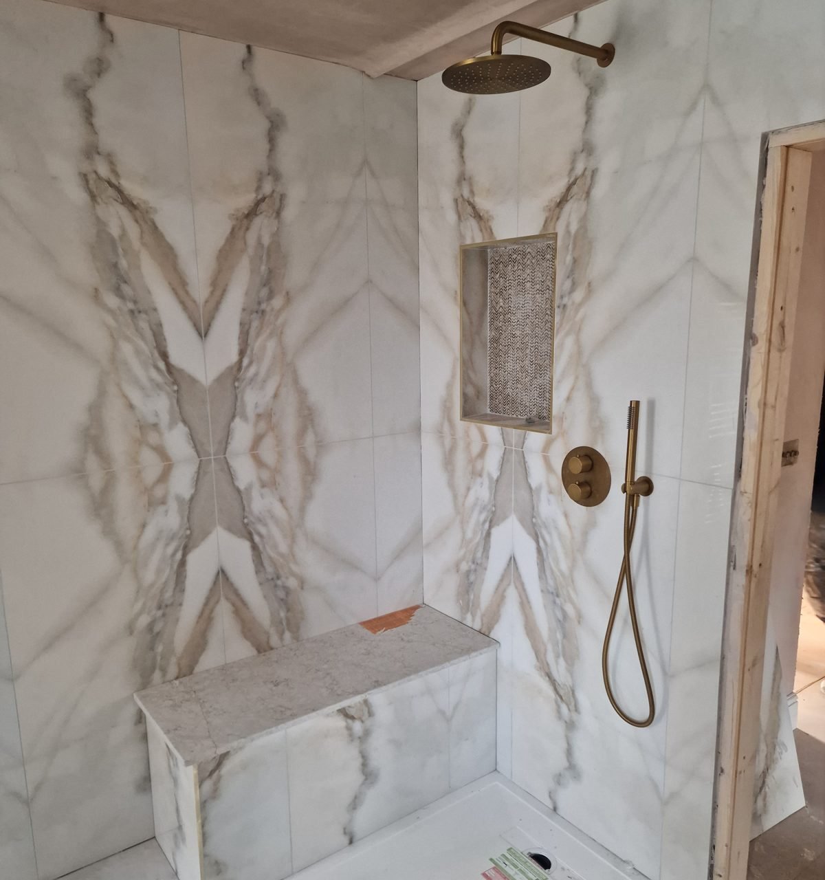 Walk-in shower in book-matched marble-effect tiles, with a tiled bench, brass rain head and recessed niche