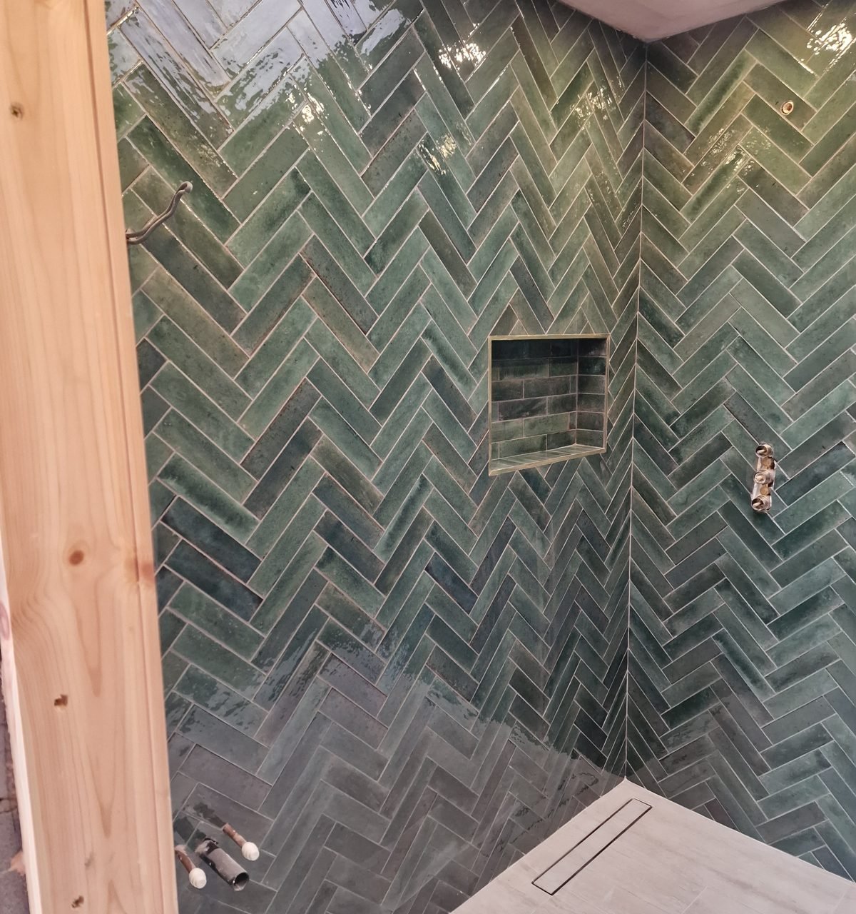 Shower lined with green glazed herringbone tiles, with a tiled niche and linear floor drain