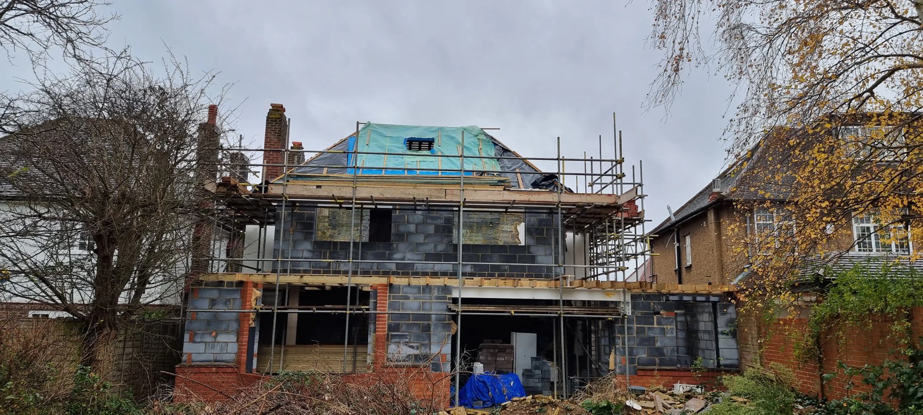 The house wrapped in scaffolding, with bare blockwork walls and the roof under temporary membrane