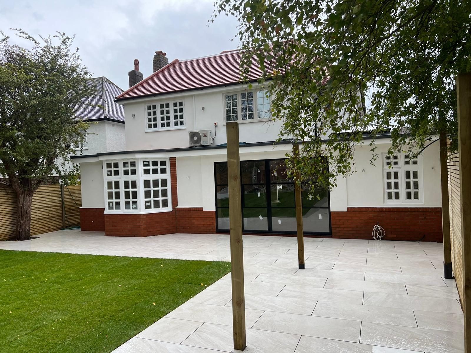 Finished rear elevation with white render, a red brick plinth, bay window and black-framed glazed doors