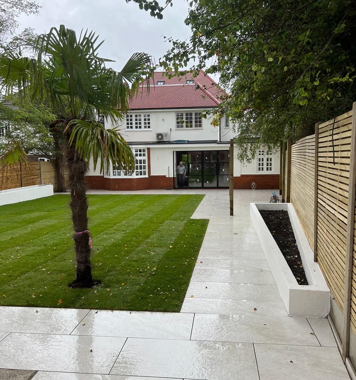 View from the end of the garden back to the house, along the porcelain path past the lawn and palm tree