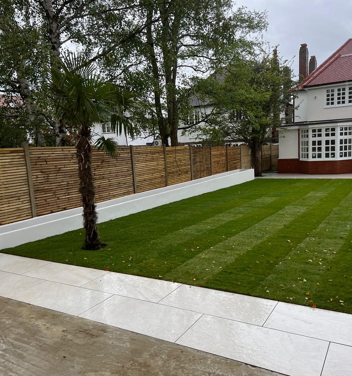 Finished garden with striped new turf, a palm tree, white rendered planters and slatted fencing