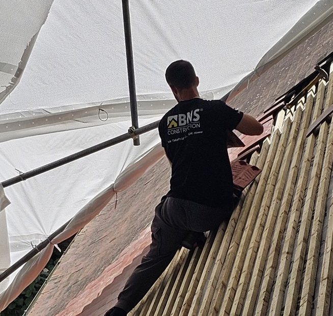 BNS roofer fixing clay tiles over new timber battens on a steep slope