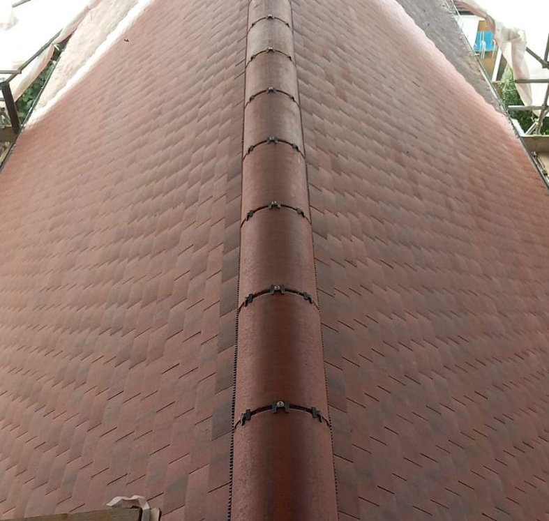 Long run of half-round ridge tiles along the finished roof, each held with a metal clip