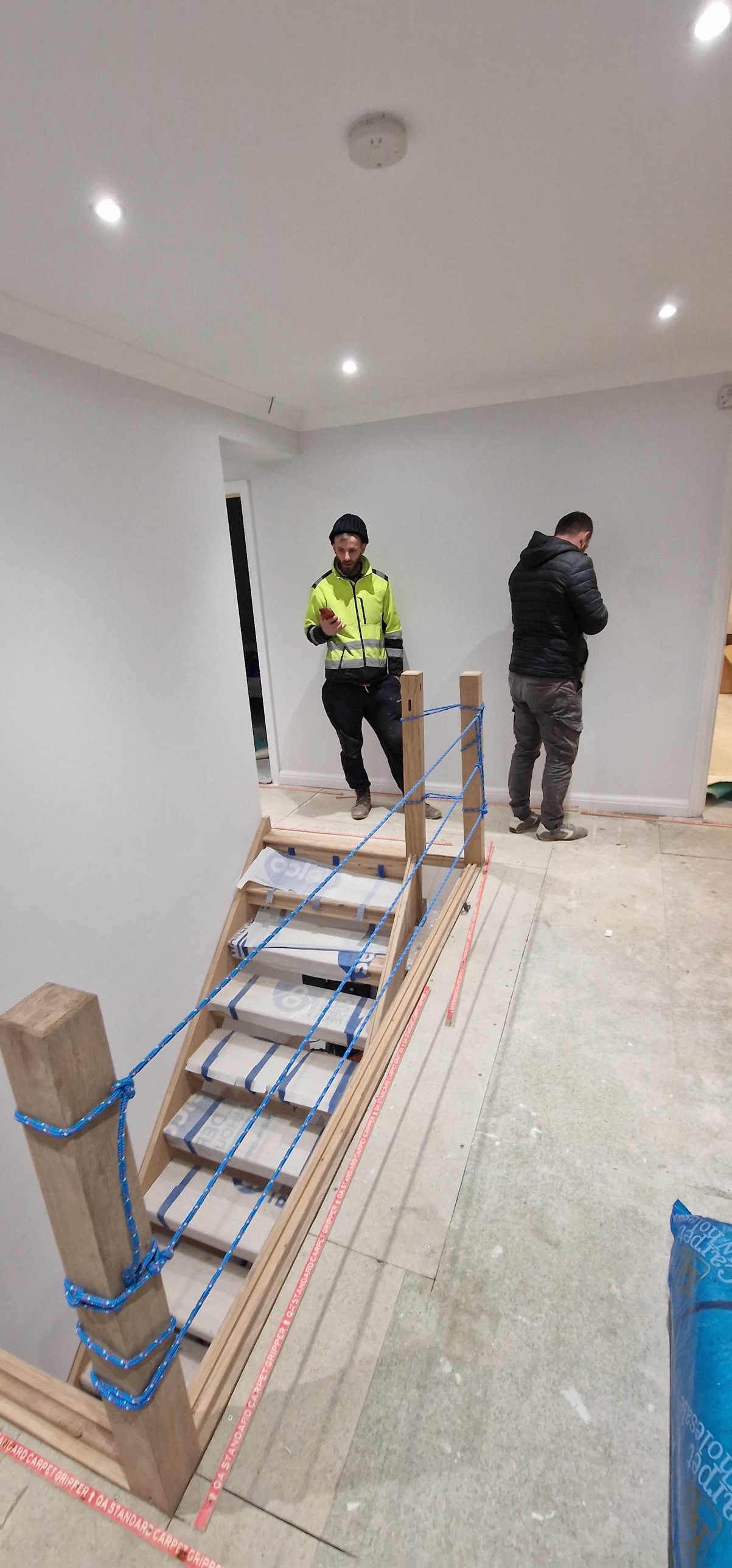 New oak staircase wrapped in protective tape, with two builders in the hallway