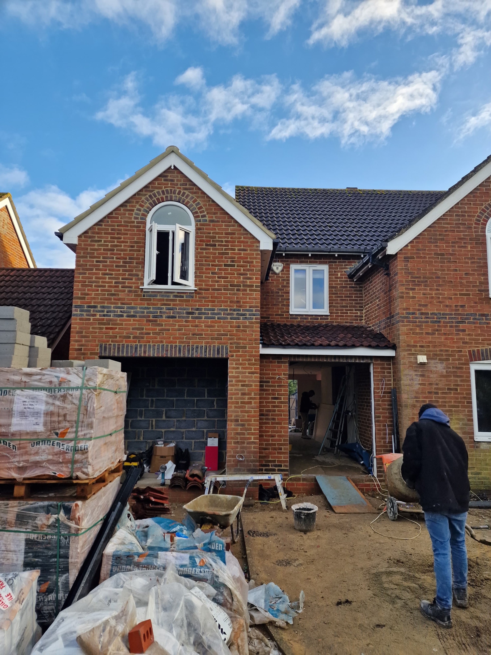Front of the house mid-build, with pallets of matching bricks and a new arched window above the garage