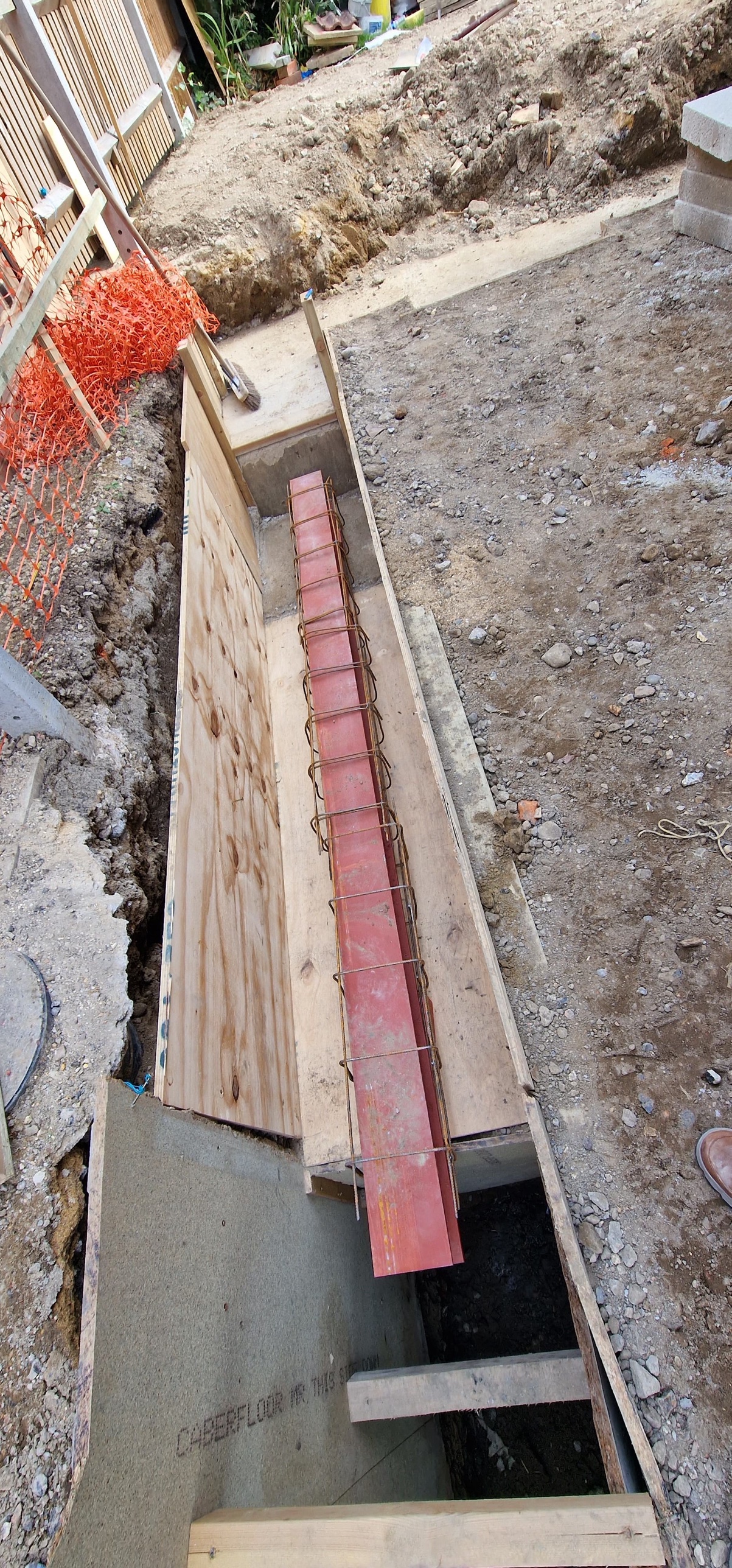 Red steel beam lying in a timber-shuttered trench, ready for the concrete ground beam