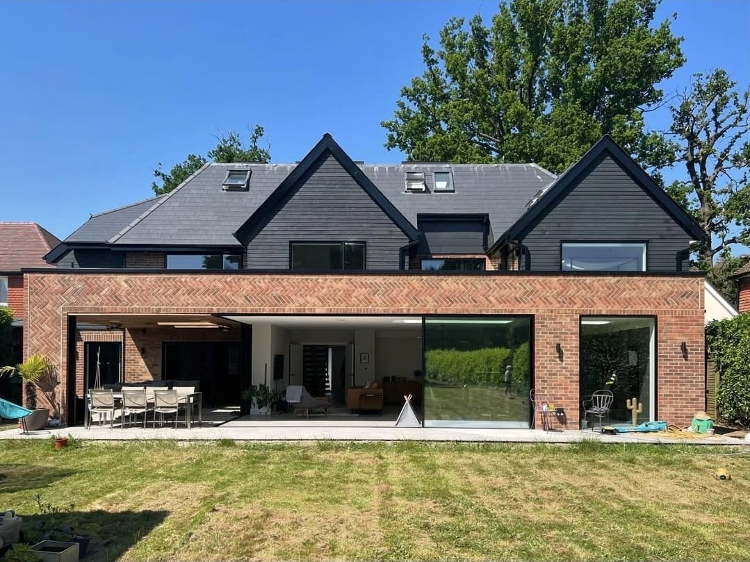 Rear of the Weybridge house, with a single-storey brick extension, wide glazed doors and black-clad gables above