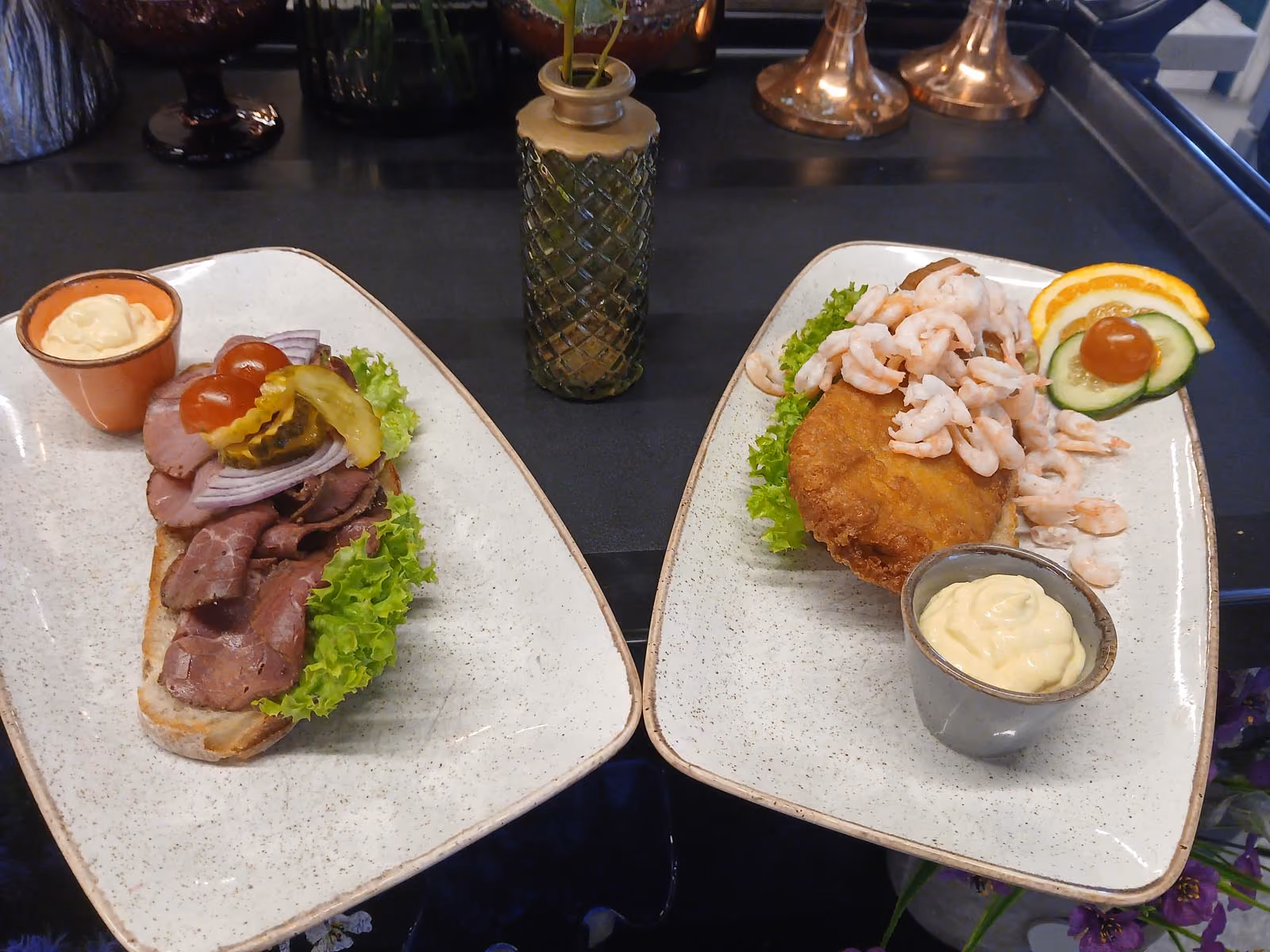 To smørbrød på tallerkener med reker, fritert fisk, roastbeef, grønnsaker og majones.