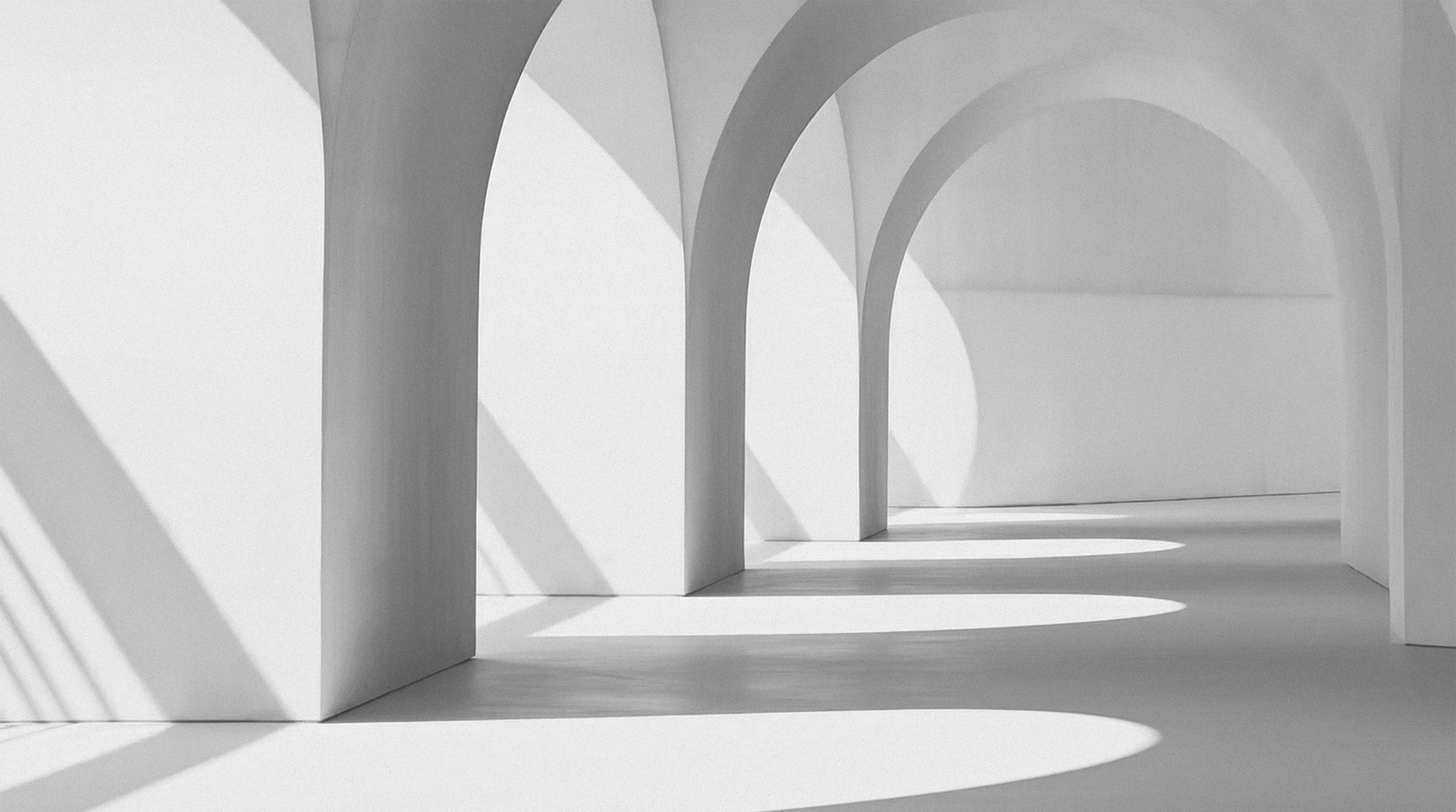 Un espace intérieur minimaliste avec plusieurs arches blanches alignées créant des ombres allongées au sol et sur les murs.