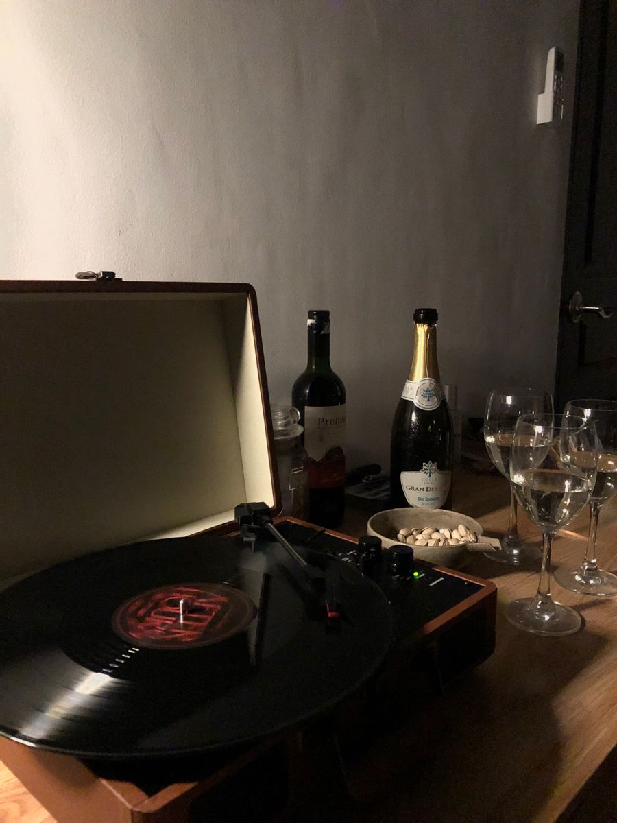 A record on the turntable beside two bottles and a row of glasses