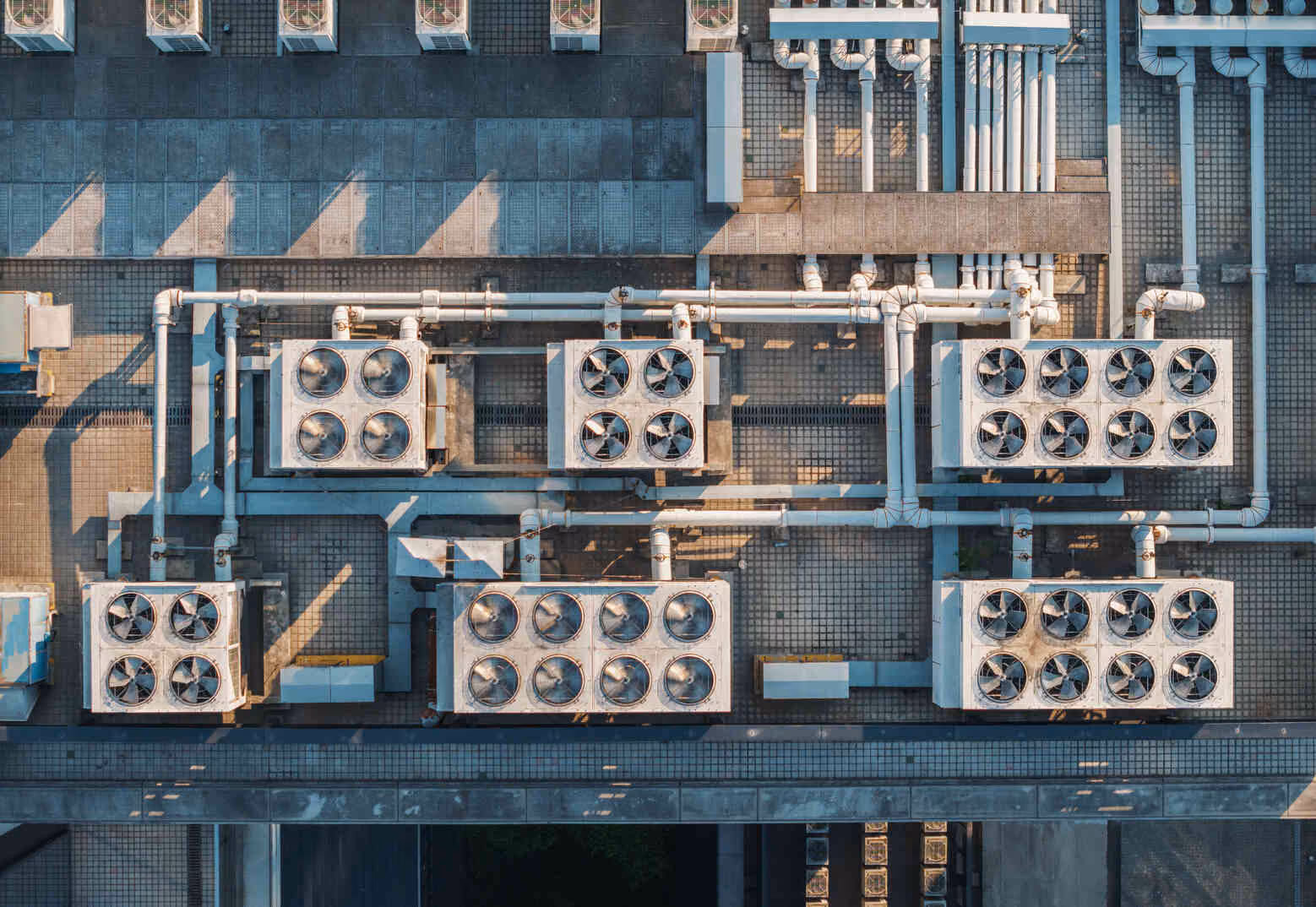 Aerial view of multiple industrial HVAC units with fans and piping arranged on a large rooftop.