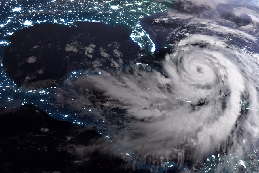 Satellite view of a large hurricane swirling over the Caribbean Sea near Florida and the Gulf of Mexico at night, with coastal city lights visible around the storm.