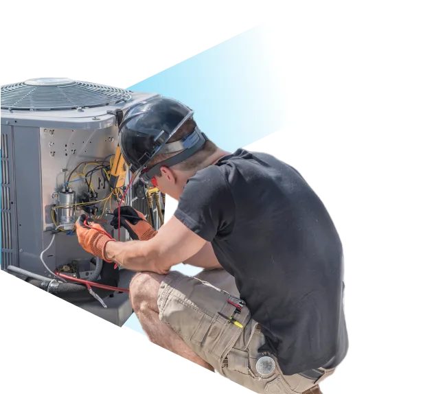 Technician wearing a black helmet and orange gloves crouches while working on the exposed wiring of an air conditioning unit outdoors against the sky.