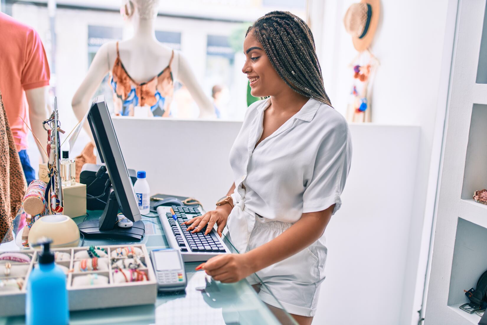 Woman standing at a retail store counter with a computer, holding a credit card and smiling while making a purchase.