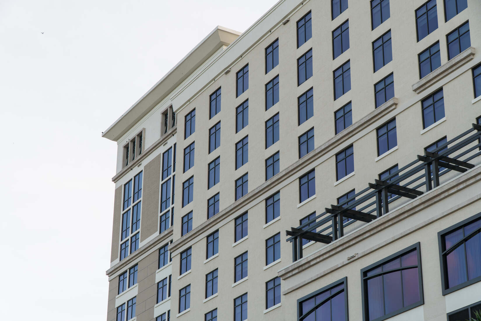 Exterior view of a modern multi-story hotel building with beige walls and many windows reflecting blue sky.