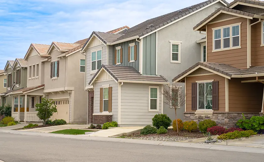 Row of modern suburban houses with varied exterior colors and designs along a clean street under a partly cloudy sky.