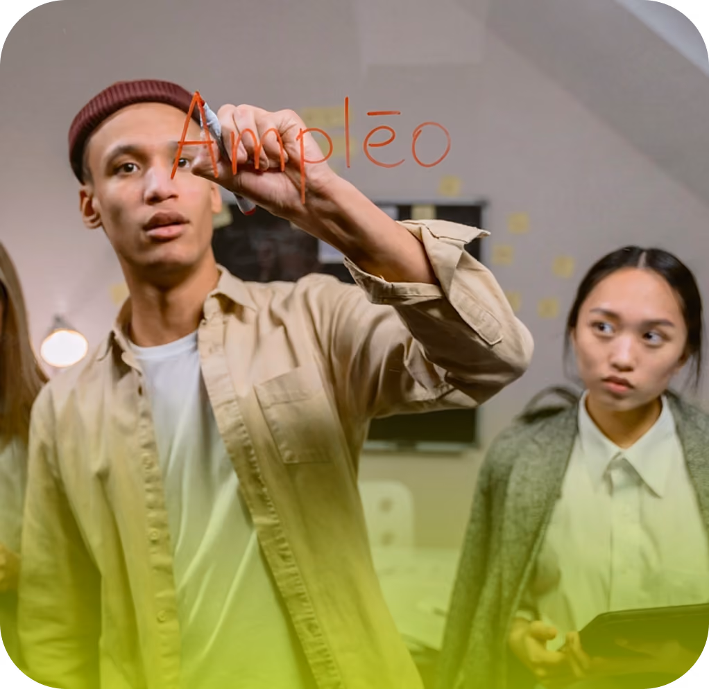 A young man wearing a beige shirt and maroon beanie writes the word "Ampleo" on a glass surface with a red marker, while a young woman in a gray jacket and white shirt looks on, holding a tablet.