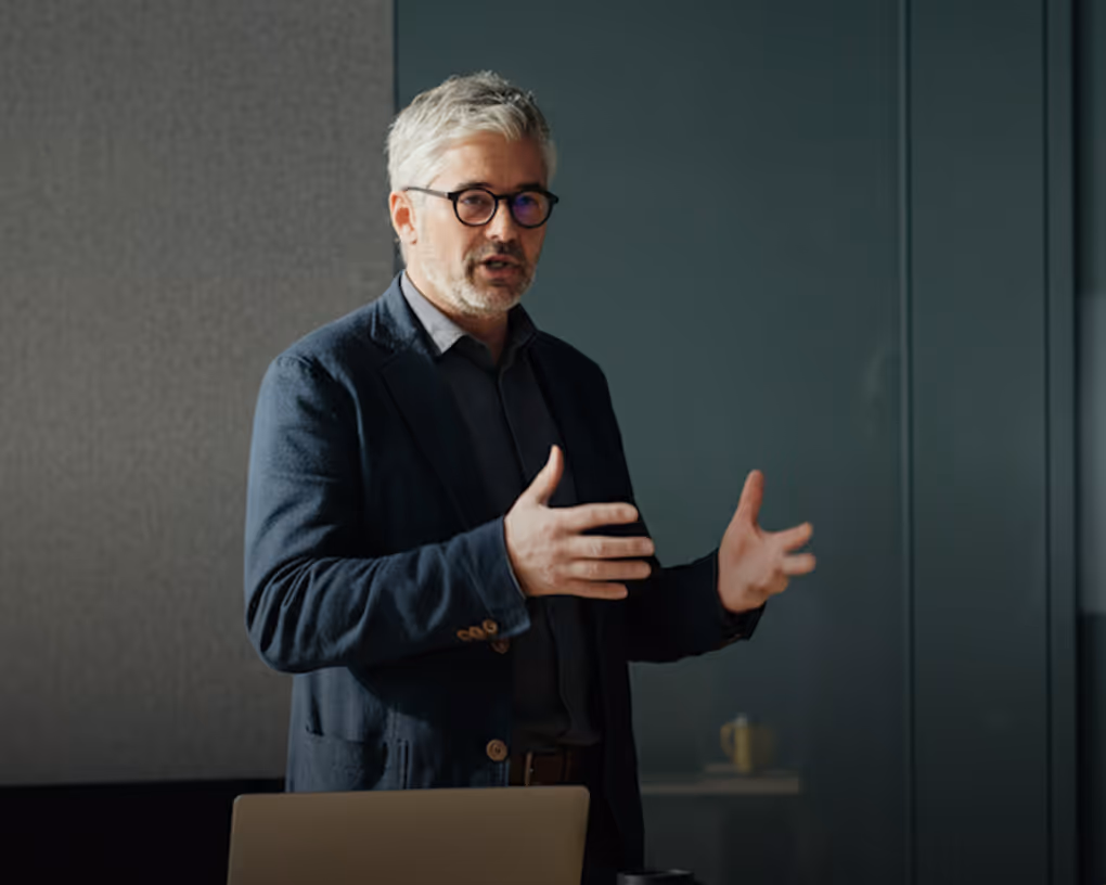 Middle-aged man with gray hair and glasses gesturing while speaking in an office setting.