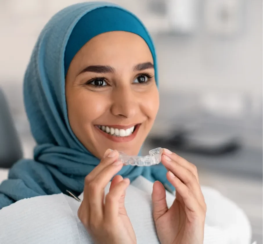 Smiling patient holding a clear aligner tray of the kind used in Invisalign treatment
