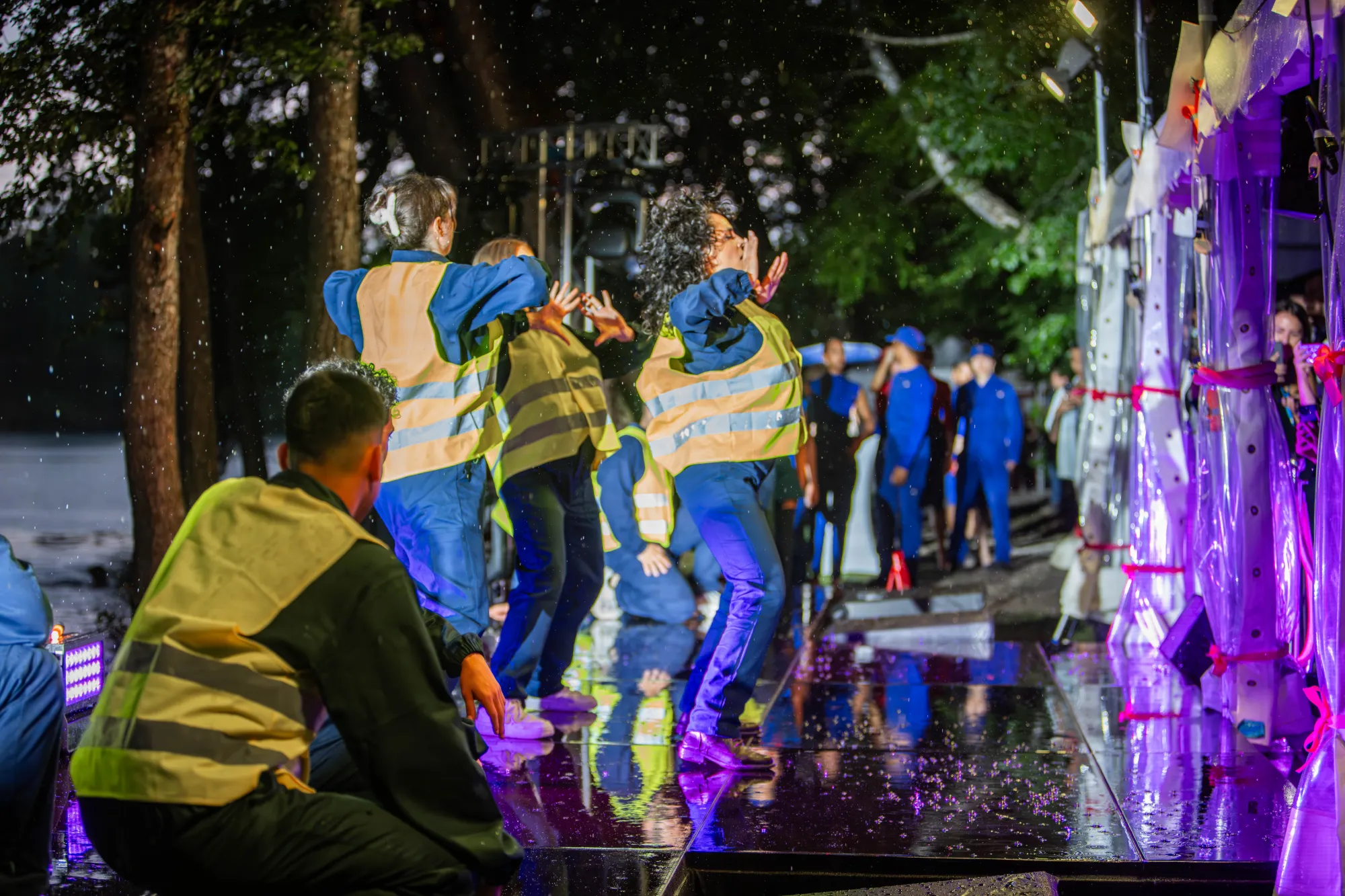 Dance performance in the rain in high-visibility vests among the trees