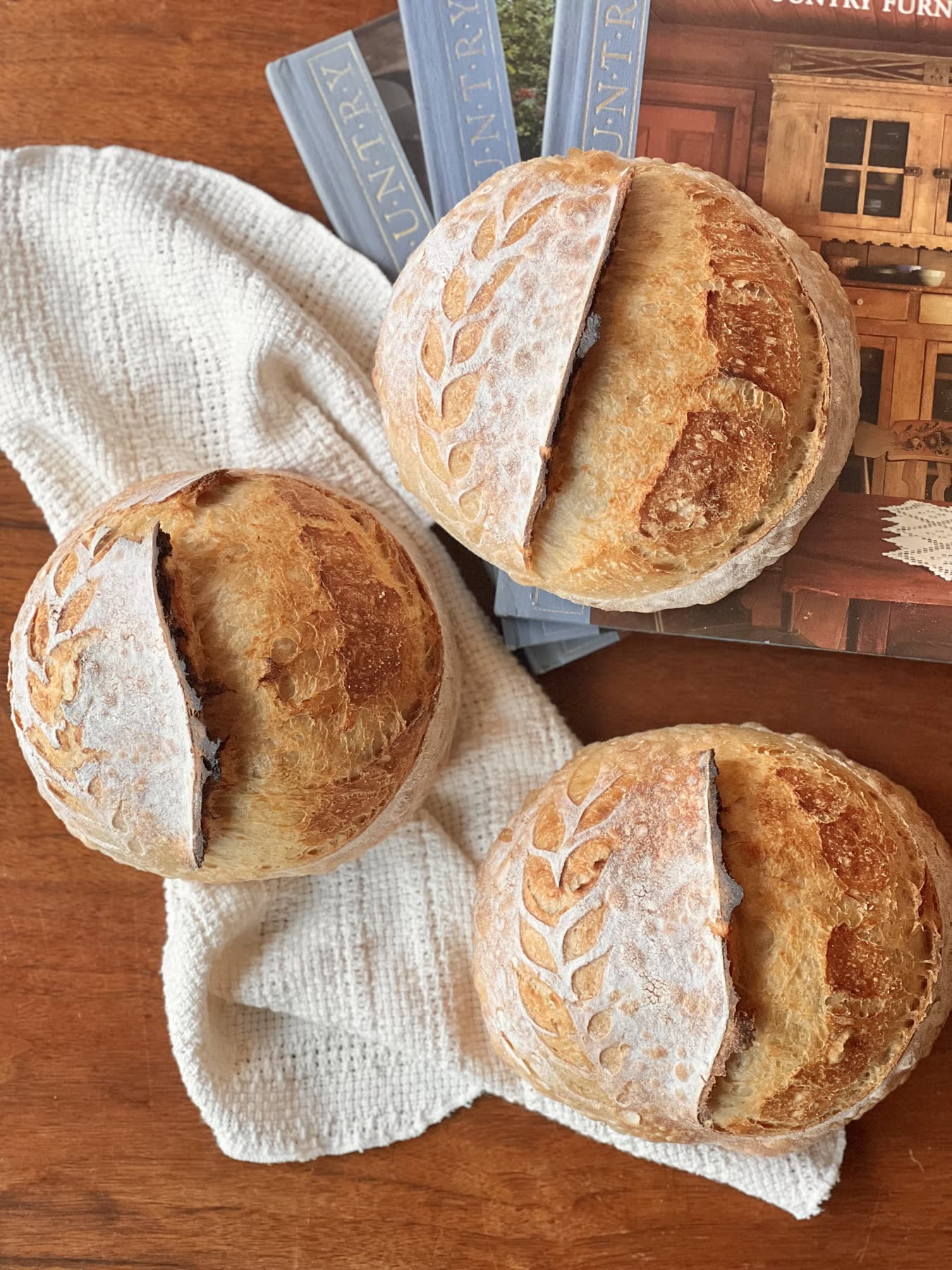 Scored organic sourdough boules cooling on a linen towel, baked by The Homespun Baker