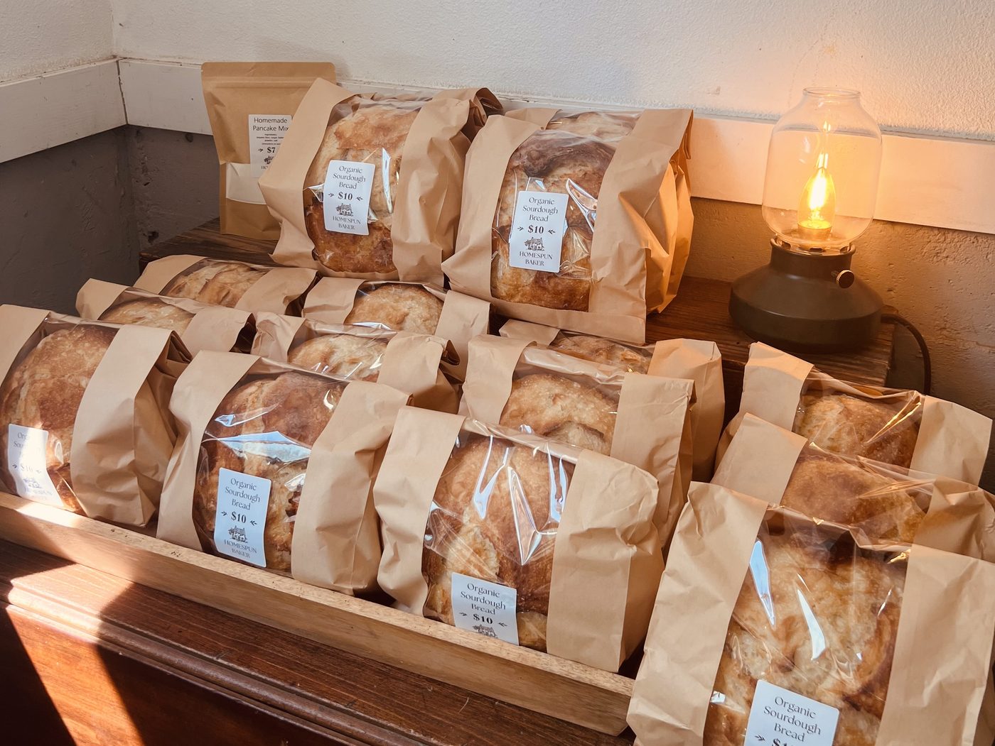 Wrapped loaves of The Homespun Baker's sourdough on the stand at Schoch Dairy, lit by a small lantern