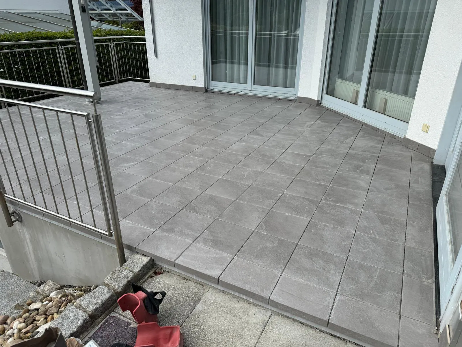 Empty gray tiled patio with stainless steel railing and glass sliding doors on a house exterior.