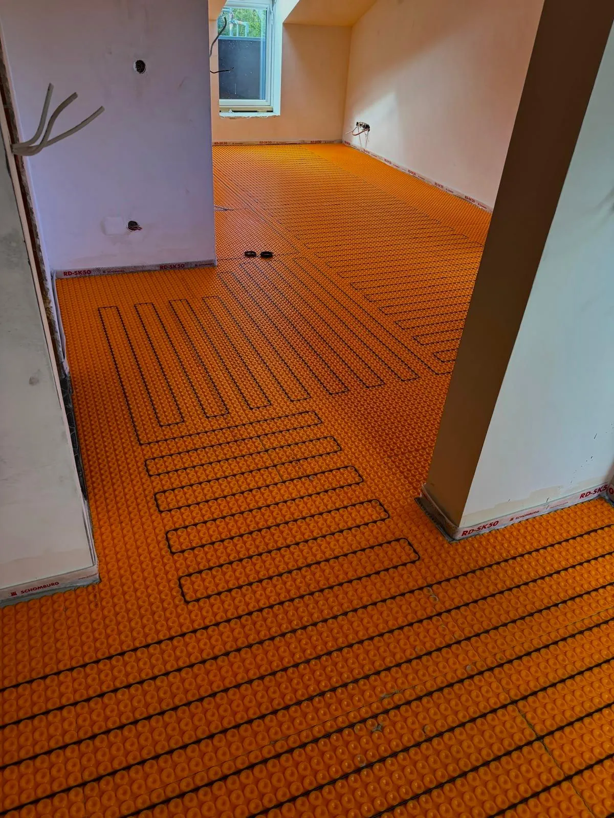 Room under construction with orange underfloor heating system installed on the floor.