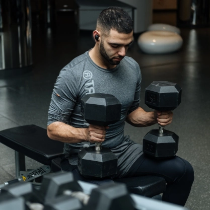 **Alt text:** Person performing seated dumbbell curls during a strength training workout at a CrossFit gym in Bakersfield, CA.