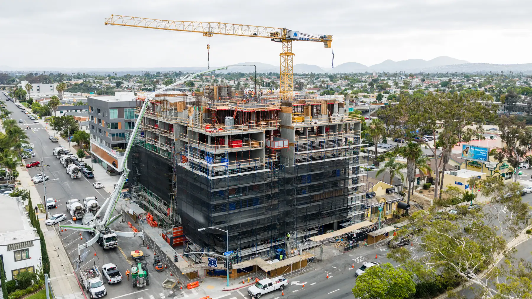 Large multi-story building under construction with cranes and scaffolding in an urban area.