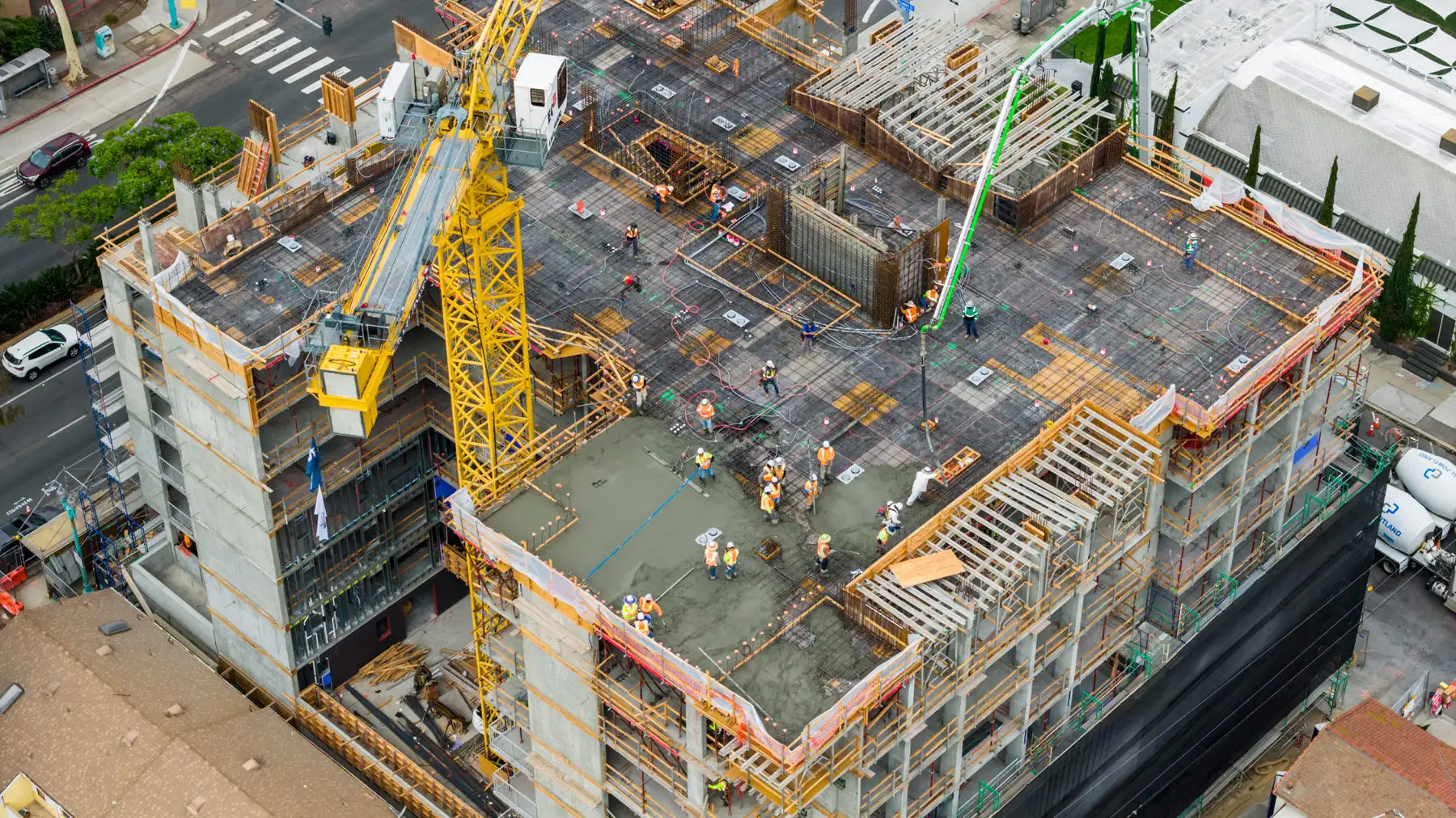 Aerial view of construction workers pouring concrete on a building under construction with crane and scaffolding.
