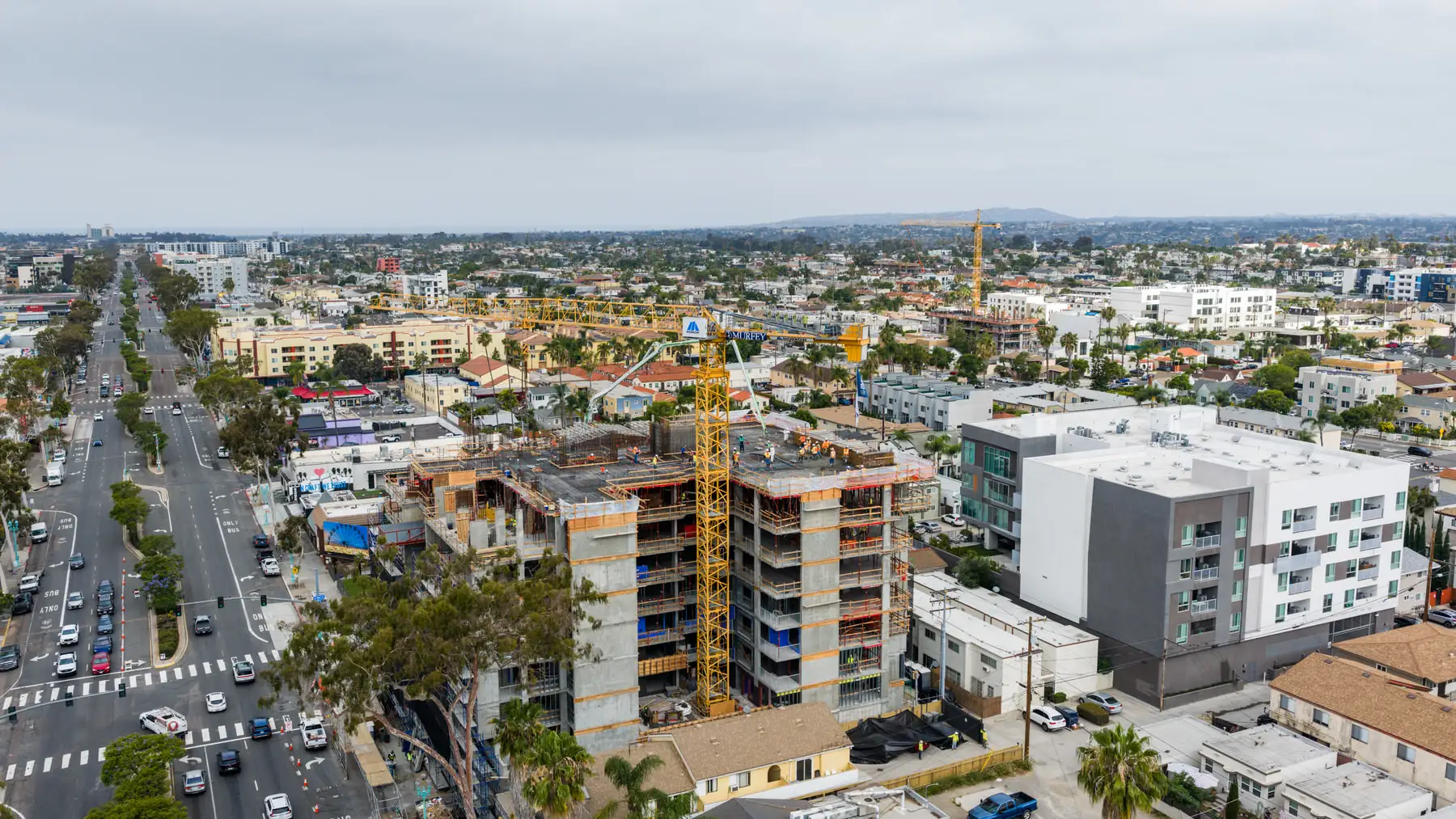 Urban construction site with a yellow crane and workers on a partially built multi-story building.