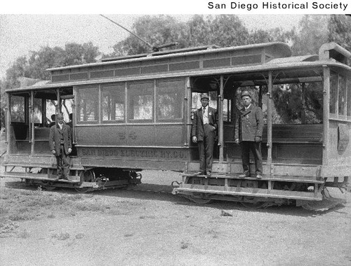 An early San Diego streetcar, with three men standing beside it.