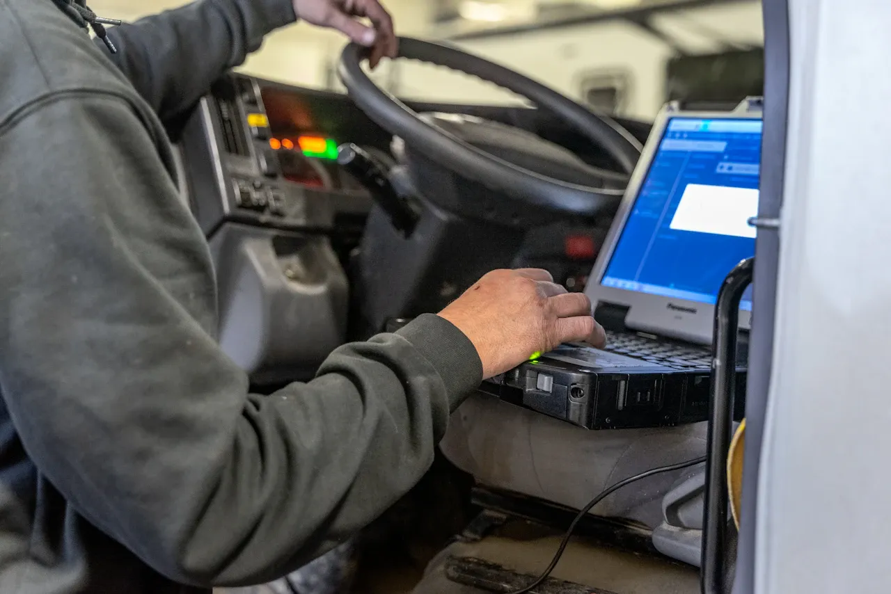 Truck diagnostics technician uses a laptop inside a heavy-duty truck cab to troubleshoot vehicle systems.