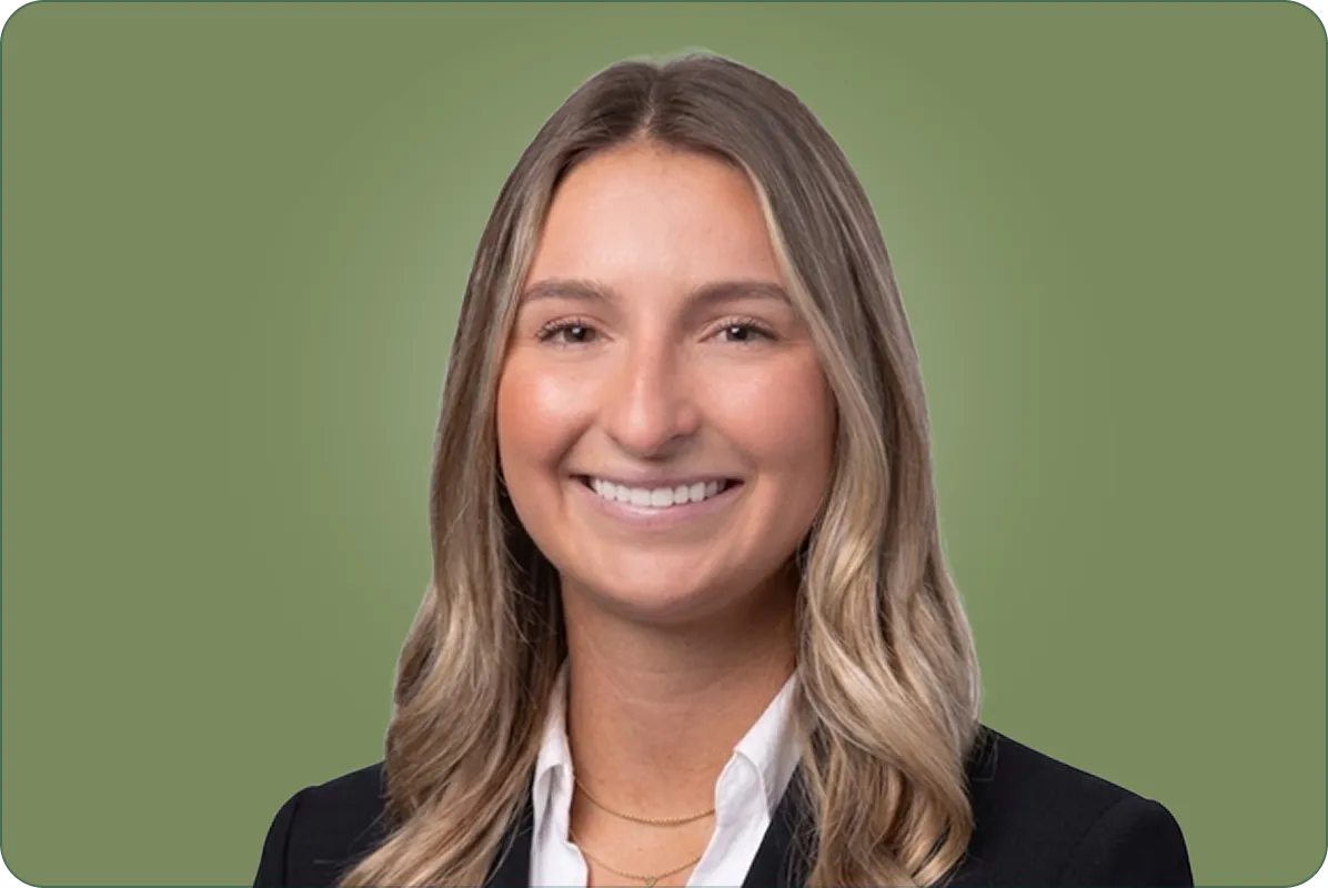 Smiling woman with long blonde hair wearing a black blazer and white shirt on green background.