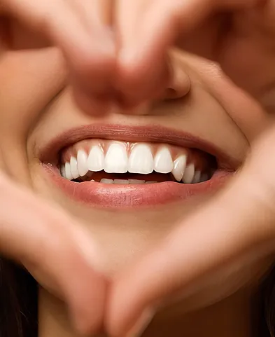 Close-up of a smiling mouth framed by hands forming a heart shape.