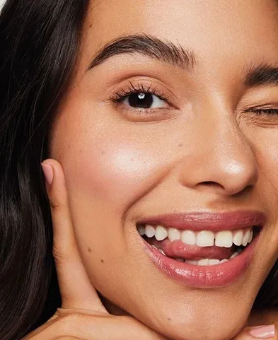 Close-up of a smiling woman winking with tongue out and finger on cheek.
