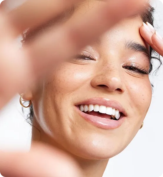 Close-up of smiling woman with natural freckles and hoop earrings reaching toward the camera.