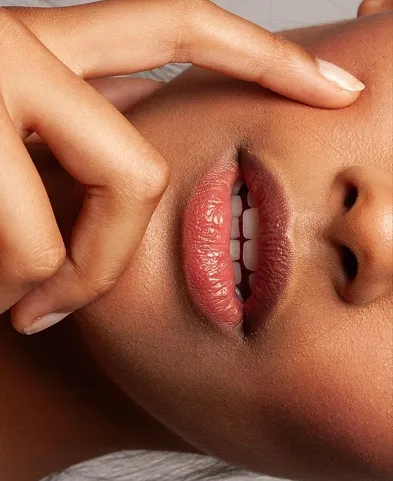 Close-up of a dark-skinned face with parted lips and a finger touching the upper lip.
