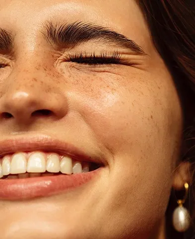 Close-up of a smiling woman with closed eyes, freckles, and a pearl earring.