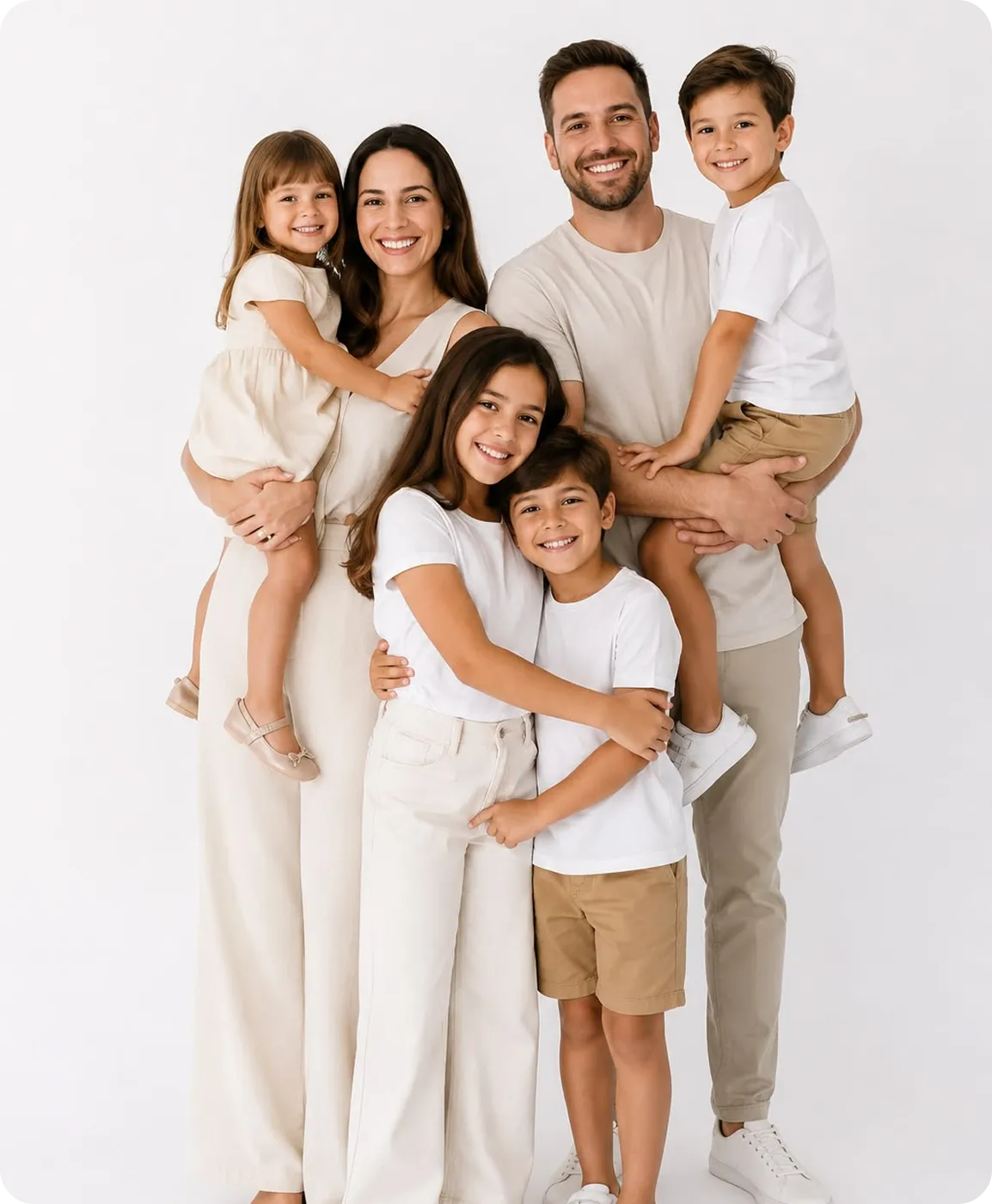 Smiling family of six with two parents holding two kids and two kids standing in front, all dressed in white and beige.