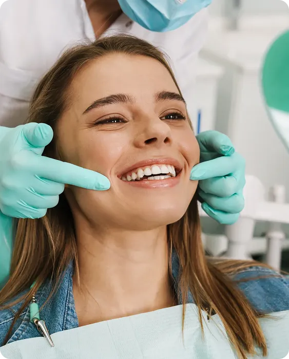 Woman smiling in dental chair as gloved dentist points to her teeth during checkup.