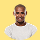 Smiling bald man with a beard wearing a white t-shirt against a yellow background.