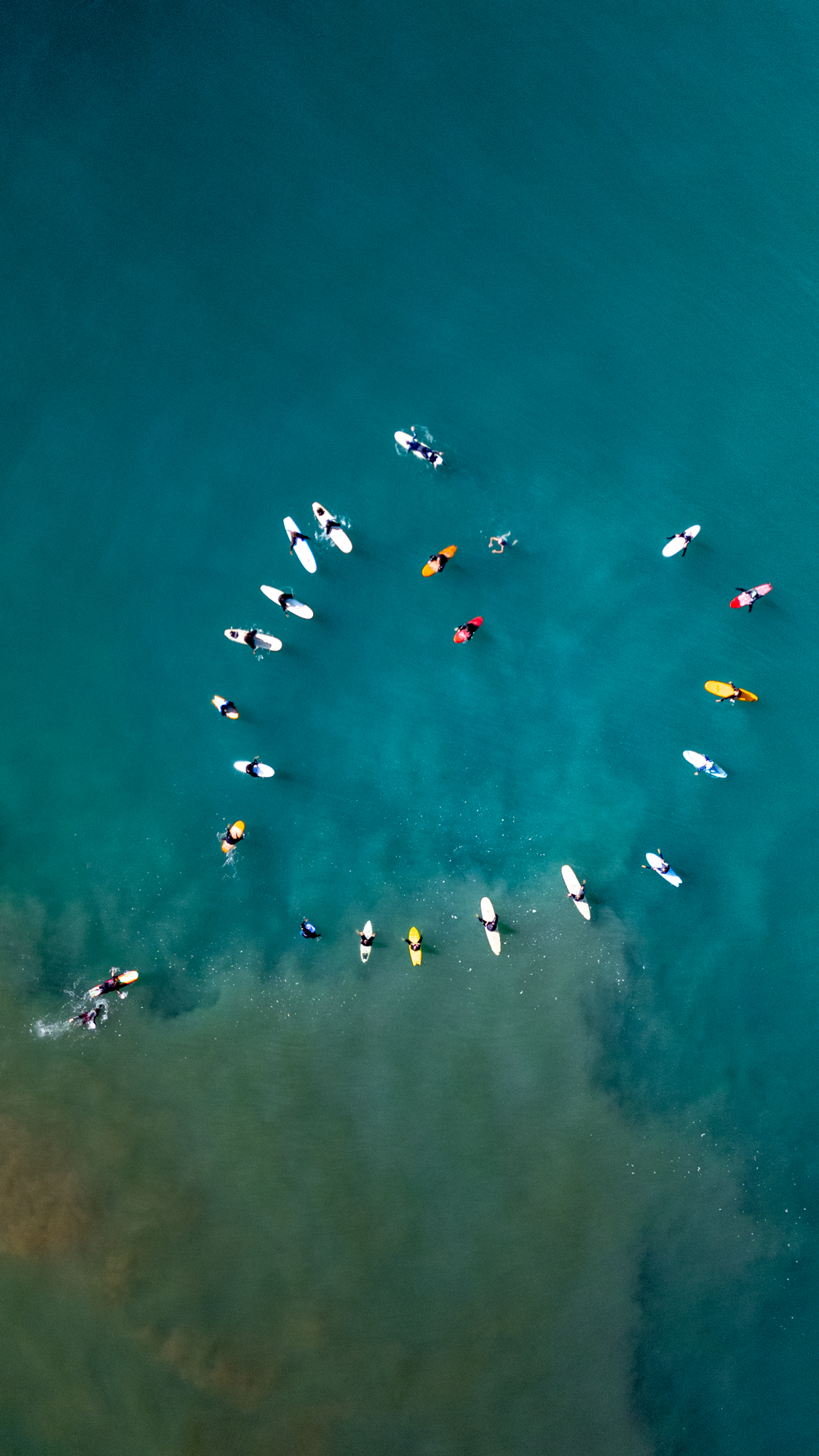 Group of surfers on surfboards forming a circle in blue ocean water near shore.