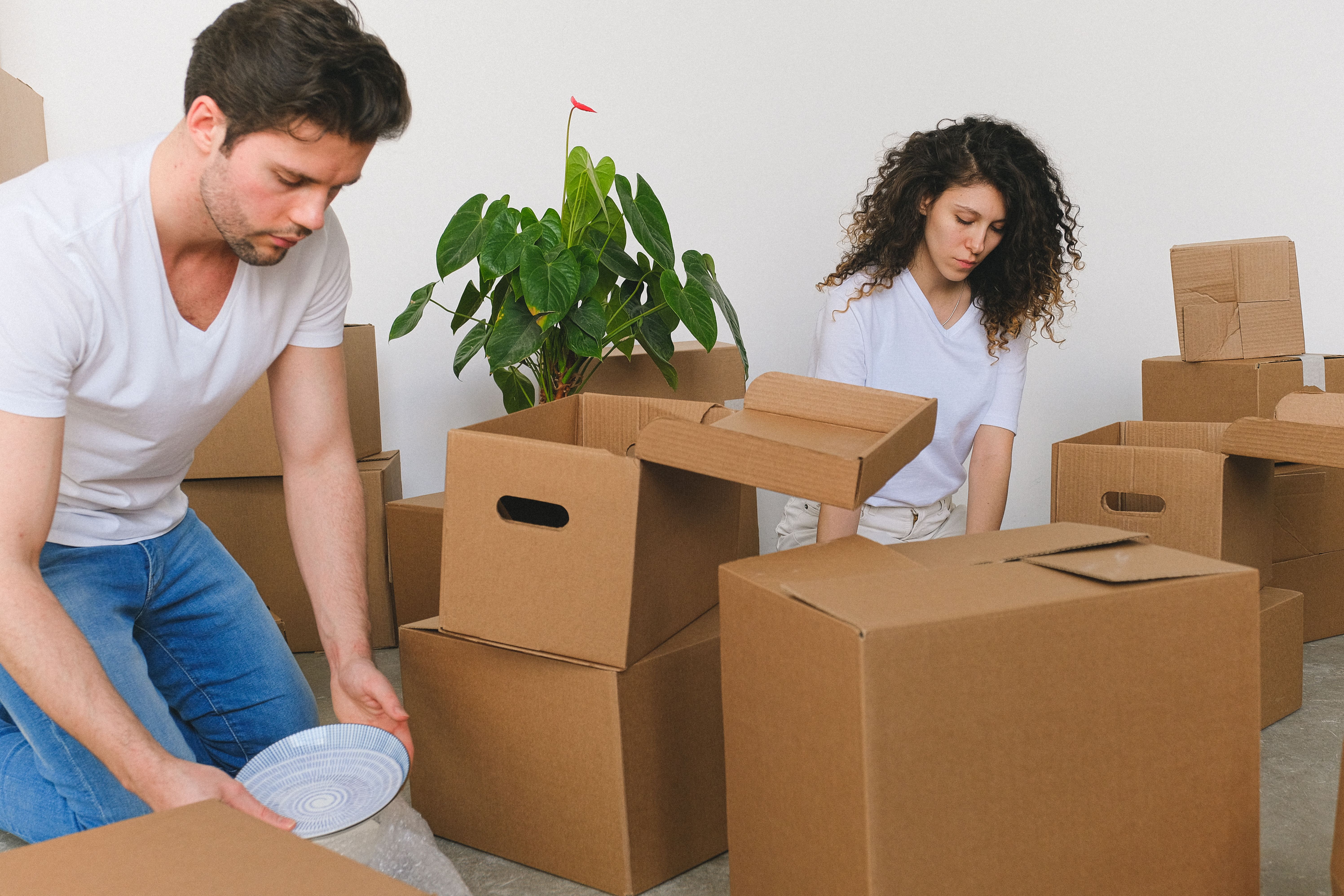 Serious young relocating man and woman packing fragile things into carton boxes while preparing for moving into a new apartment