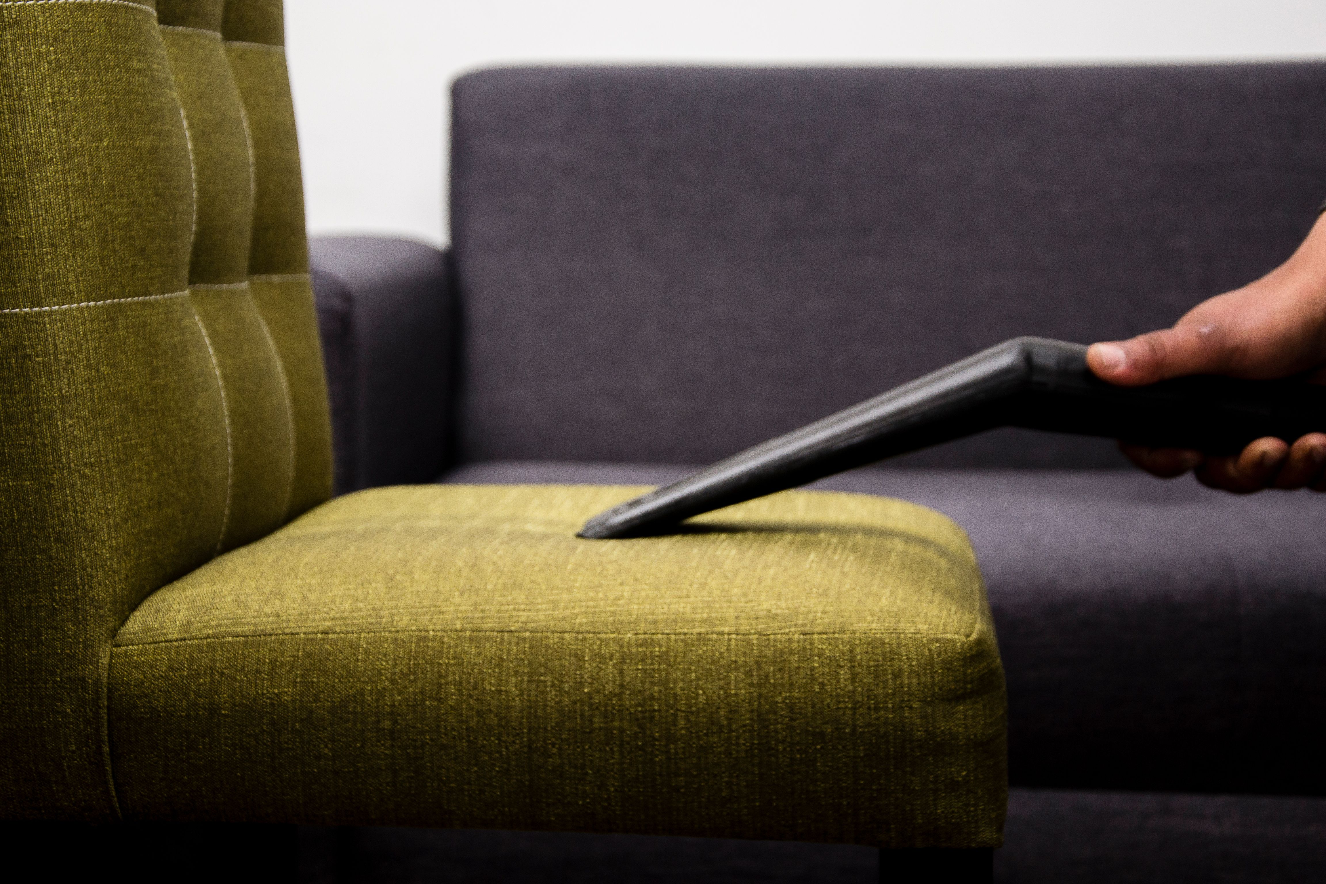 Close-up of a person vacuuming a modern sofa chair indoors