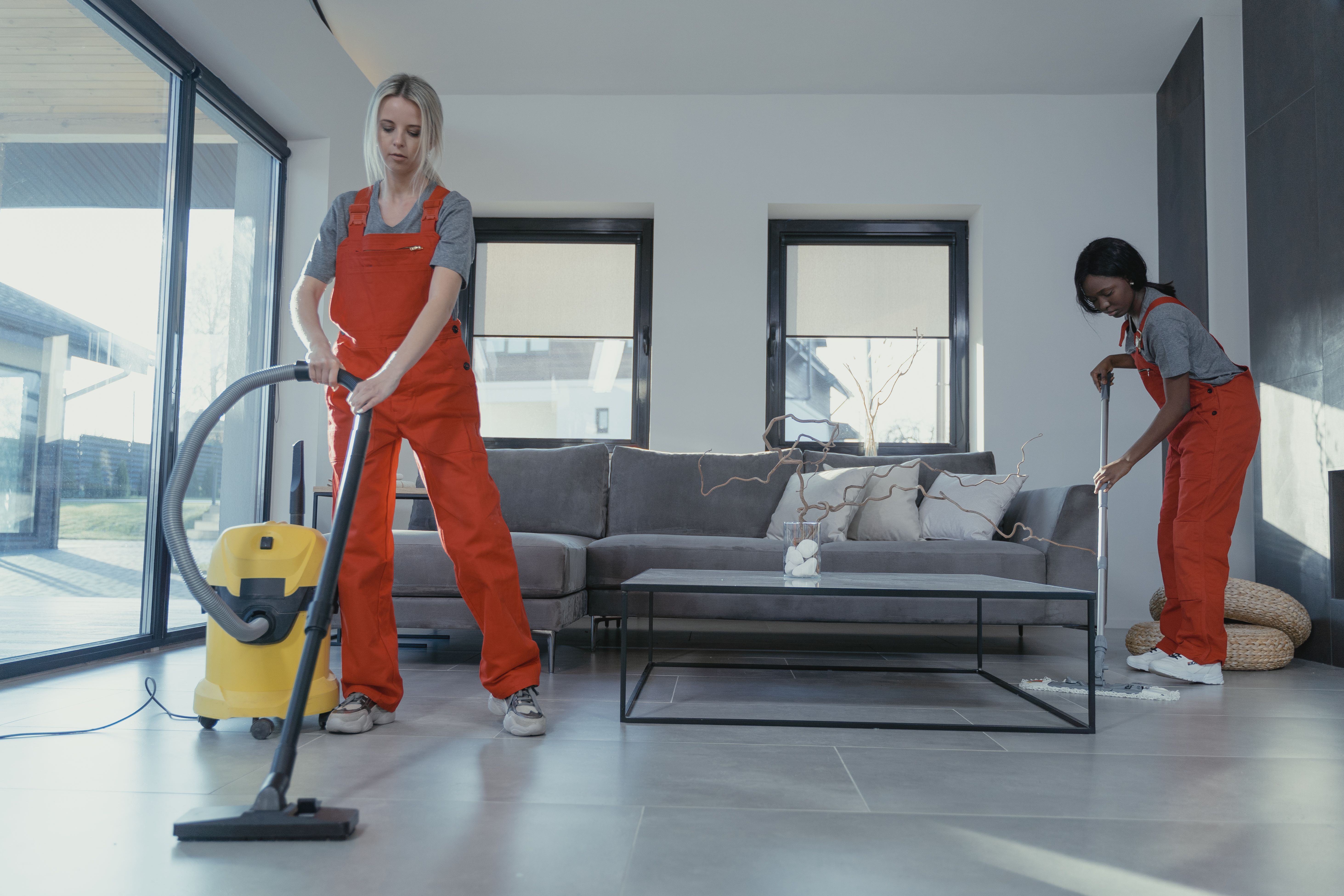 Two people in overalls vacuuming and sweeping a modern living room