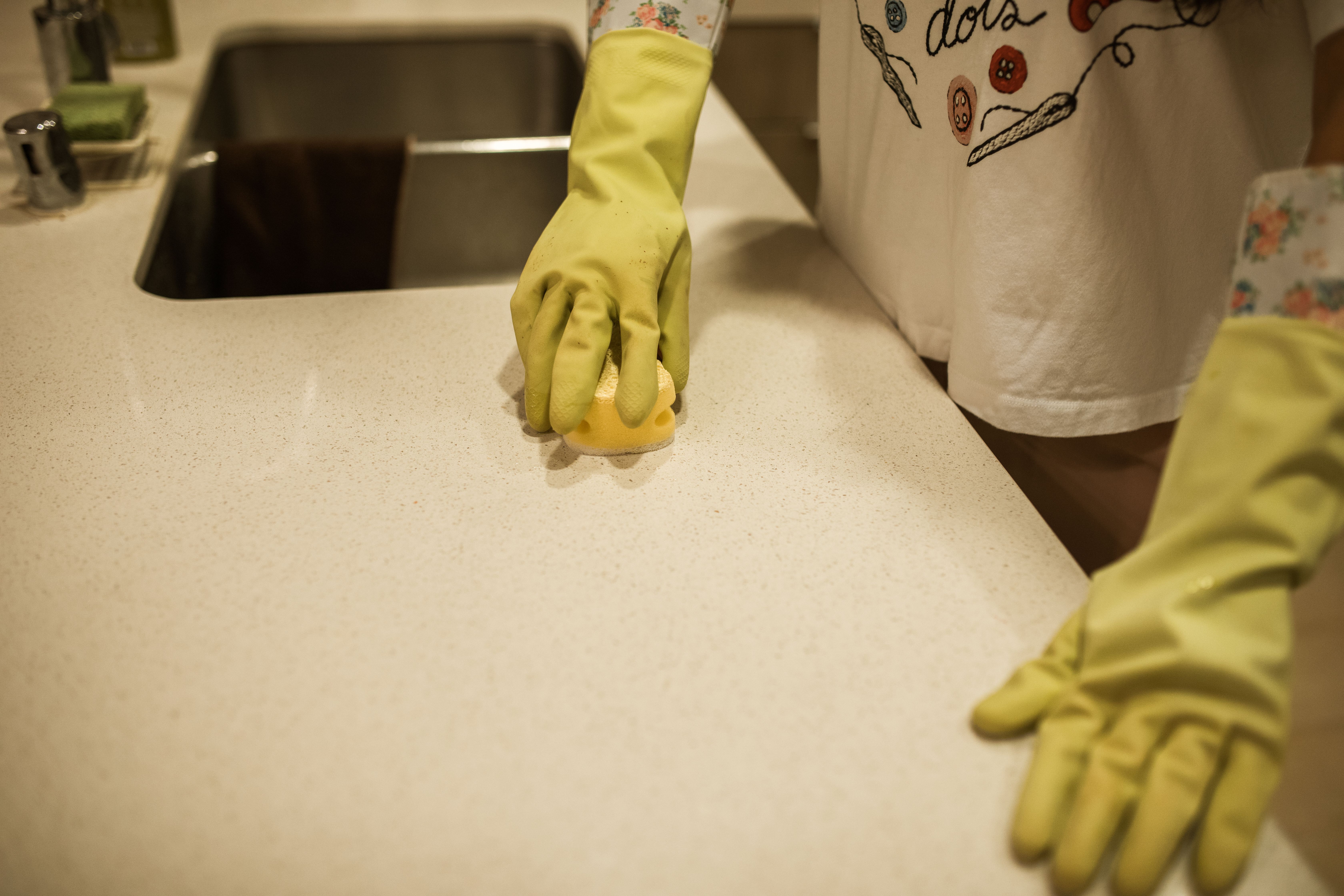 A person using yellow rubber gloves to clean a kitchen counter with a sponge