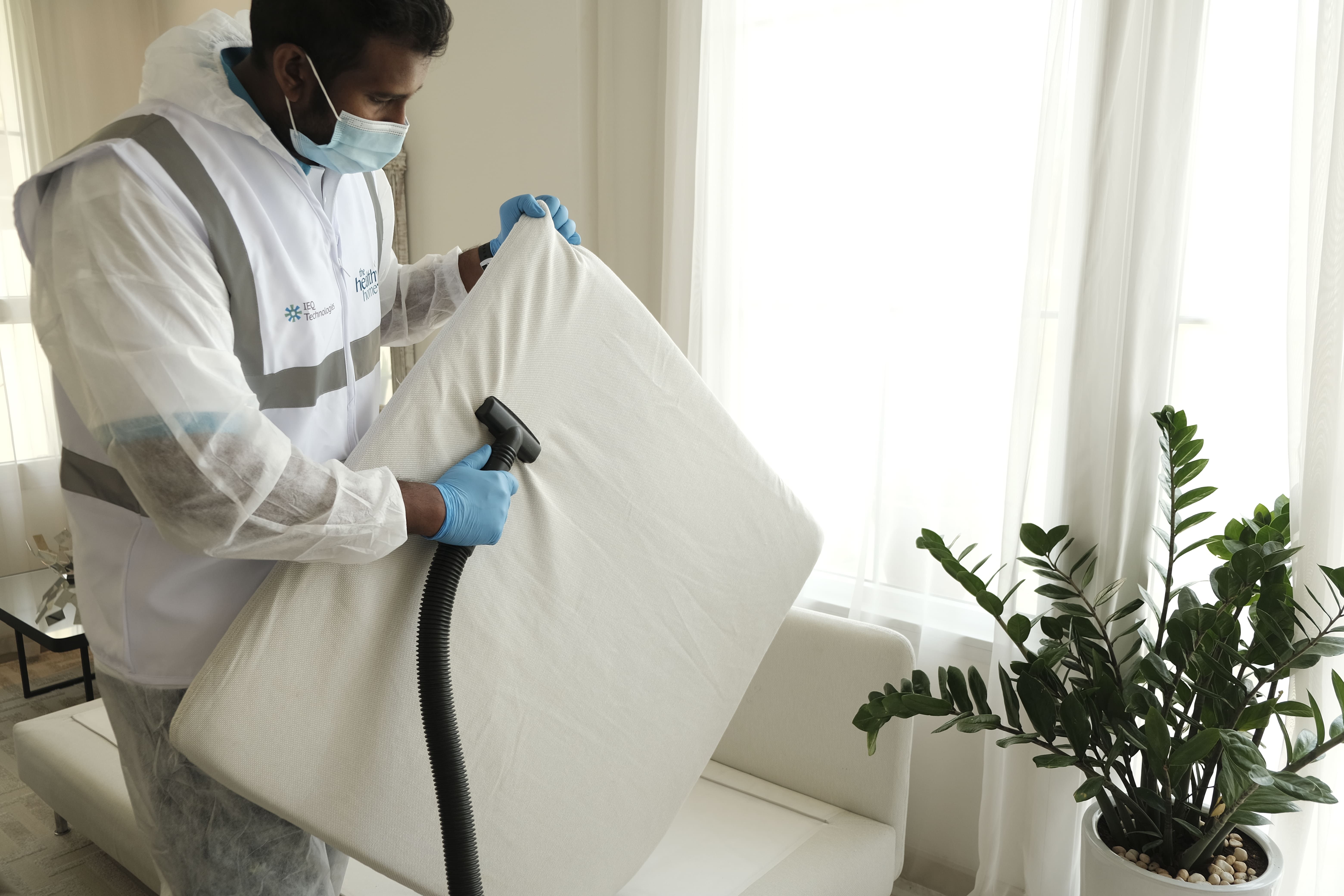 A cleaner in protective gear vacuuming a mattress during a deep clean.
